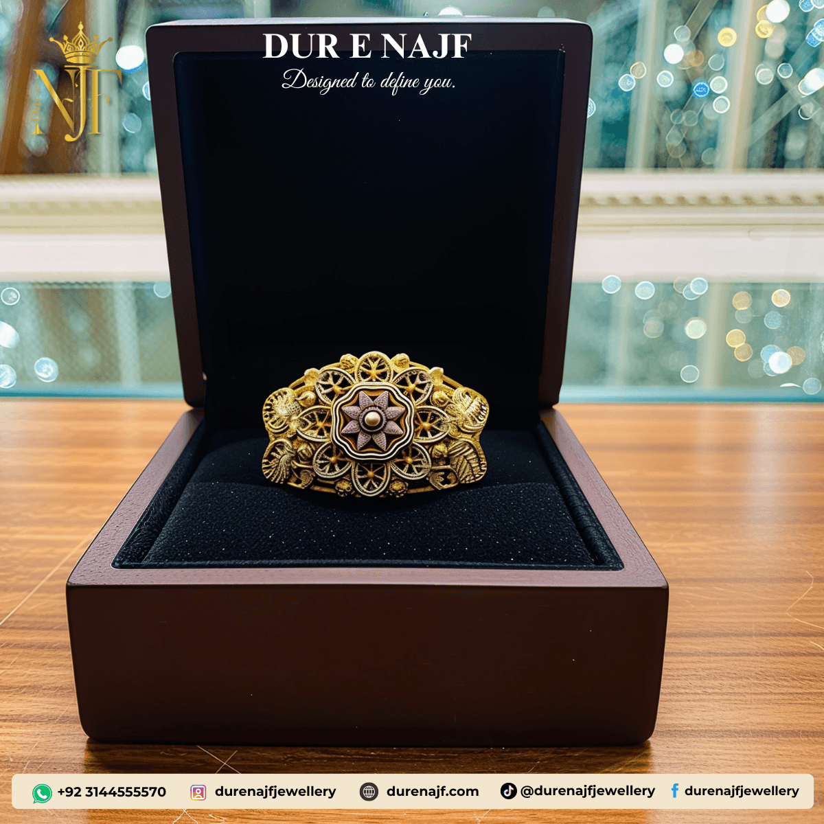 Wide artificial fashion ring with an ornate gold-tone filigree band and a prominent central medallion design in mixed metallic finishes, presented in a dark wood jewelry box.