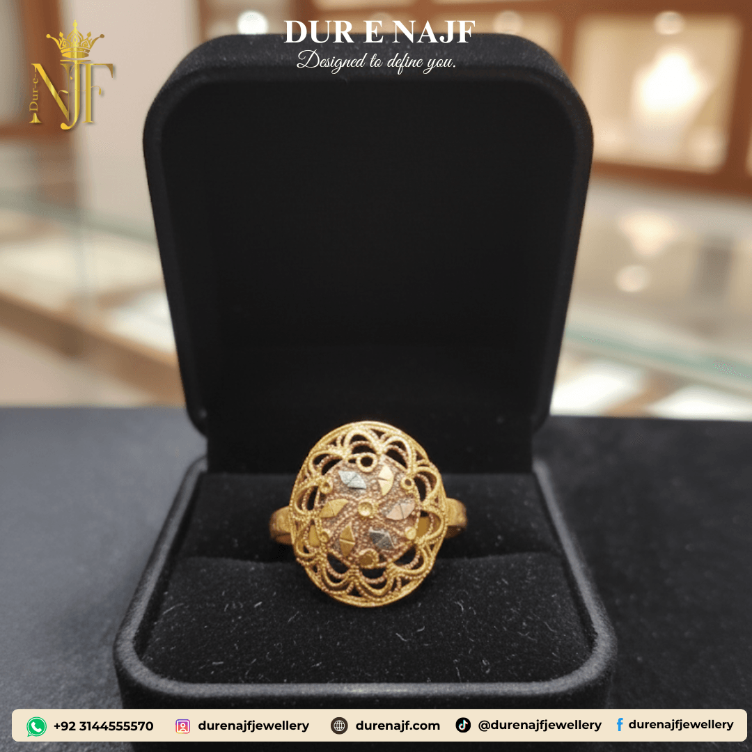 Oval-shaped artificial jewelry ring with intricate gold-tone filigree metalwork and a central patterned design in mixed metallic finishes, displayed in a black velvet ring box.