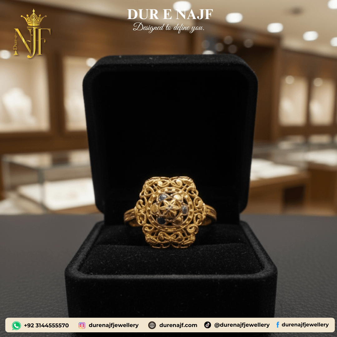 Antique-style gold-tone artificial ring with elaborate filigree scrollwork surrounding a central cluster of small, dark blue accent stones, displayed in a black jewelry box.